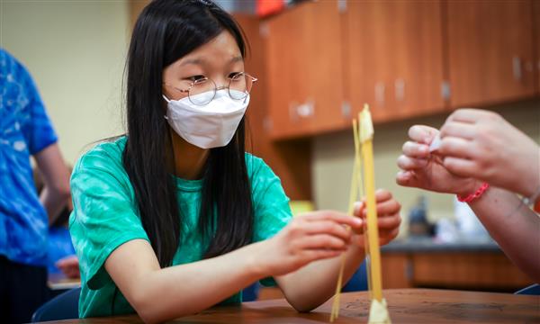 A girl adds to a spaghetti tower